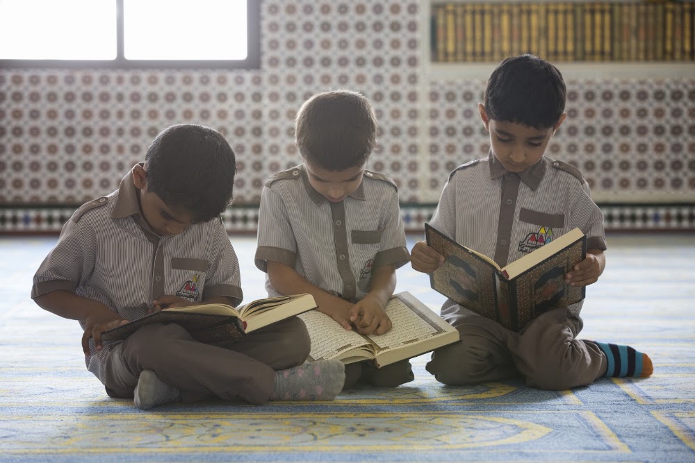 ثلاثة أطفال يجلسون على السجاد ويقرؤون المصحف